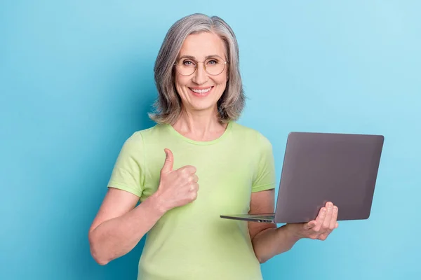 Foto di positivo affascinante donna anziana tenere per mano il computer fare pollice su isolato su sfondo di colore blu — Foto Stock