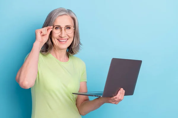 Foto di allegra felice donna anziana indossare occhiali tenere per mano il computer isolato su sfondo di colore blu — Foto Stock