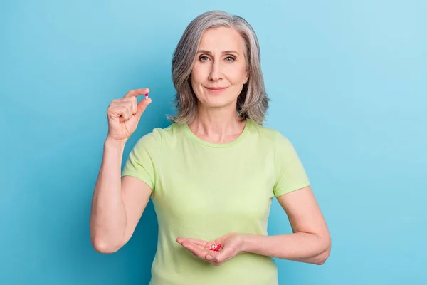 Foto di positivo affascinante donna anziana tenere mano pillole meds corona isolato su sfondo di colore blu pastello — Foto Stock