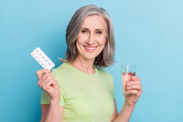 Bild av ganska trevlig charmig gammal kvinna hålla handen glas vatten piller isolerade på pastell blå färg bakgrund — Stockfoto