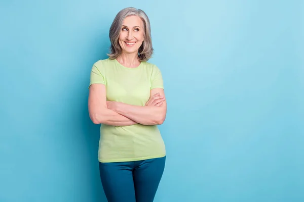 Foto van dromerig gelukkig mooi oud vrouw armen gevouwen blik leeg ruimte glimlach geïsoleerd op blauwe kleur achtergrond — Stockfoto