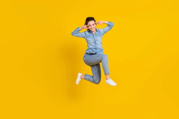 Comprimento total tamanho do corpo foto jovem menina bonita pulando para cima mostrando v-sinal gesto sorrindo isolado vívido cor amarela fundo — Fotografia de Stock