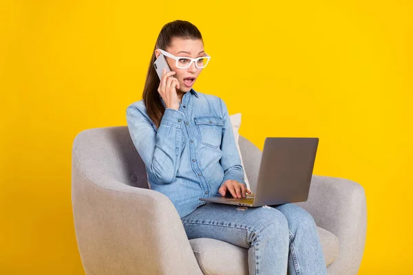 Porträtt av attraktiva förvånad trendiga flicka sitter på stol med bärbar dator ringer klient isolerad över ljusgul färg bakgrund — Stockfoto