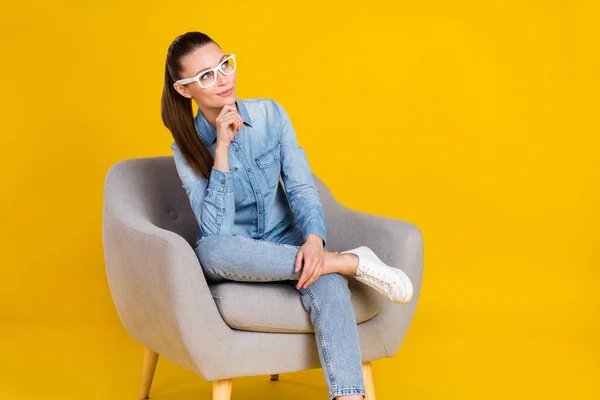Zdjęcie pewność siebie słodkie kobieta nosić dżinsowe okulary siedzi krzesło ramię podbródek patrząc puste miejsce odizolowane żółty kolor tło — Zdjęcie stockowe