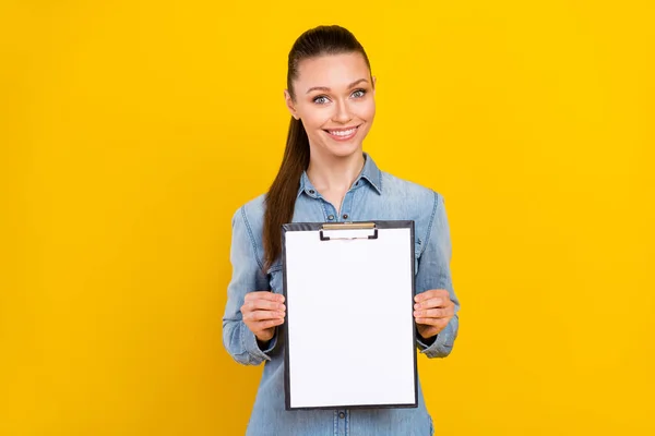 Photo portrait woman showing clipboard with empty space smiling isolated vivid yellow color background copyspace — Foto Stock