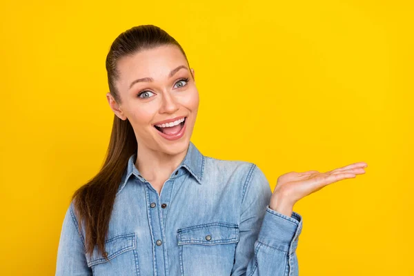 Foto van opgewonden glanzende jonge dame gekleed jeans shirt open mond houden arm lege ruimte glimlachen geïsoleerde gele kleur achtergrond — Stockfoto