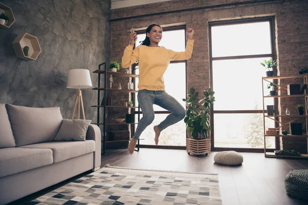 Foto van gelukkige mooie jonge vrouw gekleed gele trui springen typinh modern apparaat rijzen vuist binnen huiskamer — Stockfoto