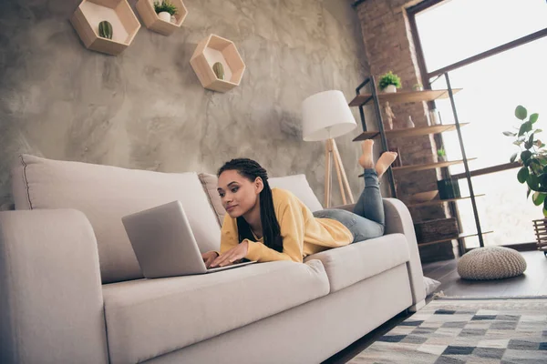 Полная длина фото сфокусированной молодой темной кожи хорошая женщина смотреть ноутбук работы лежат диван в доме в помещении — стоковое фото