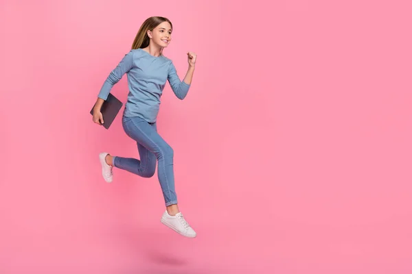 Повнорозмірна фотографія профілю молодої дівчини, що стрибає бігун, швидко виглядає порожнім простором, тримаючи ноутбук курси ізольовані на фоні рожевого кольору — стокове фото