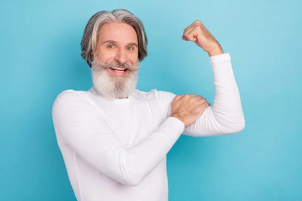 Retrato de atractivo alegre hombre de pelo gris fuerte tocando los músculos del bíceps aislados sobre fondo de color azul brillante — Foto de Stock