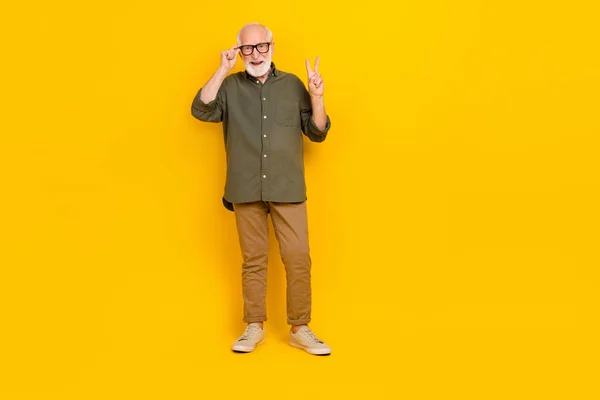 Full size portrait of cheerful satisfied aged person touch glasses show v-sign isolated on yellow color background — 图库照片