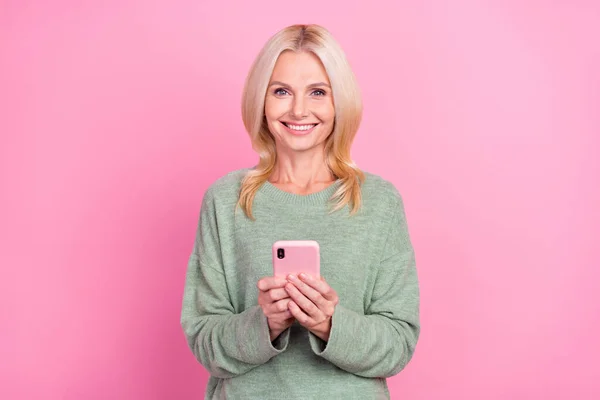 Foto di ottimista vecchia signora bionda tenere telefono usura grigio pullover isolato su sfondo di colore rosa — Foto Stock