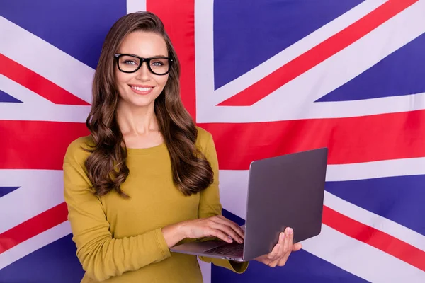 Foto de dama encantadora positiva mantenga la cámara netbook inalámbrica aislada en el fondo de la bandera británica —  Fotos de Stock