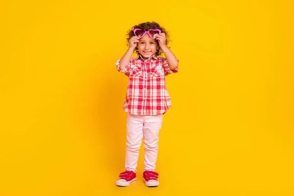 Photo of cute pretty school girl dressed checkered clothes arms heart spectacles smiling isolated yellow color background — Stockfoto