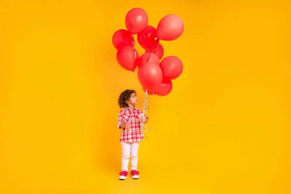 Foto di abbastanza sognante ragazza della scuola vestita vestiti a scacchi in possesso di palloncini rossi sorridente isolato colore giallo sfondo — Foto Stock