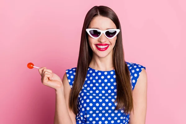 Фото молодой привлекательной женщины счастливой позитивной улыбкой держать сладкий леденец конфеты носить солнцезащитные очки изолированы на розовом фоне — стоковое фото