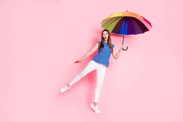 Вид в полный рост на привлекательную жизнерадостную веселую коричневолосую девушку с зонтиком в руках, развлекающуюся на розовом цветовом фоне — стоковое фото
