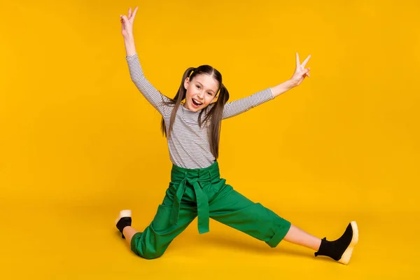 Полное фото тела молодой девушки счастливой позитивной улыбки акробатика гибкий показать мир прохладно V-знак изолирован на желтом фоне цвета — стоковое фото
