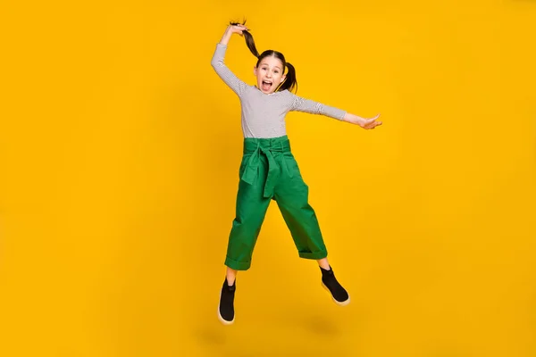 Pełna długość zdjęcie młodej podekscytowanej dziewczyny szkoły skakać trzymać kucyk odizolowany na żółtym tle kolor — Zdjęcie stockowe