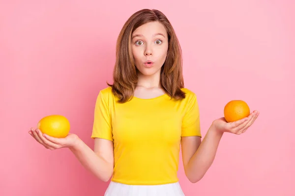 Etkilenmiş kahverengi saçlı genç kızın portakal tutan fotoğrafı pembe arka planda sarı tişört giyiyor. — Stok fotoğraf