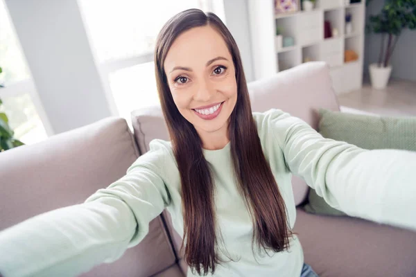 Фото довольно блестящей зрелой женщины носить бирюзовый пуловер улыбаясь сидя диван запись видео в помещении комната — стоковое фото