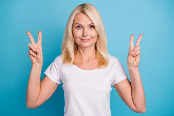 Photo of attractive aged lady showing both hands arms v-sign symbols wear casual white t-shirt isolated blue color background — стоковое фото