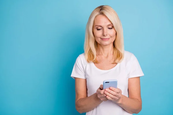 Foto di positivo moderno vecchia donna uso smart phone usura bianco t-shirt isolato su sfondo di colore blu — Foto Stock