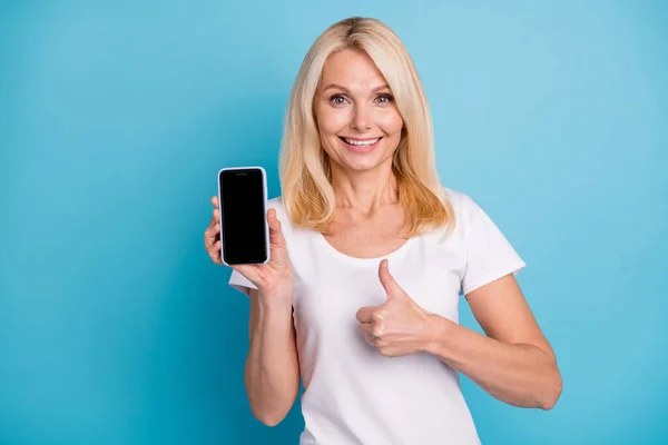 Olumlu yaşlı bayan akıllı telefonu tut baş parmak yukarı işareti seç beyaz tişört giy izole edilmiş mavi arkaplan — Stok fotoğraf