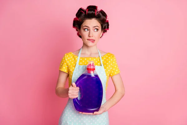 Unsure girl hold wash powder bottle bite lips look copyspace hesitate wear yellow dotted t-shirt isolated pastel color background — Stock Photo, Image