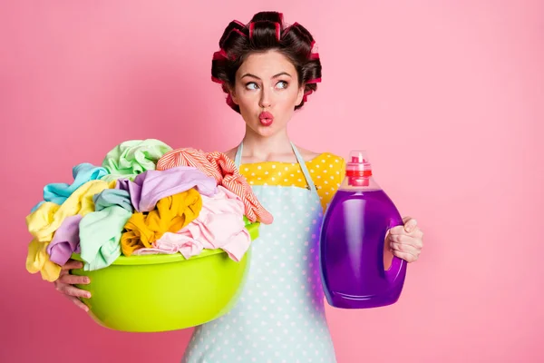 Здивована дівчина покоївка виглядає тримати брудний одяг миття басейну пляшки порошку одягу футболки ізольовані на пастельному кольоровому фоні — стокове фото