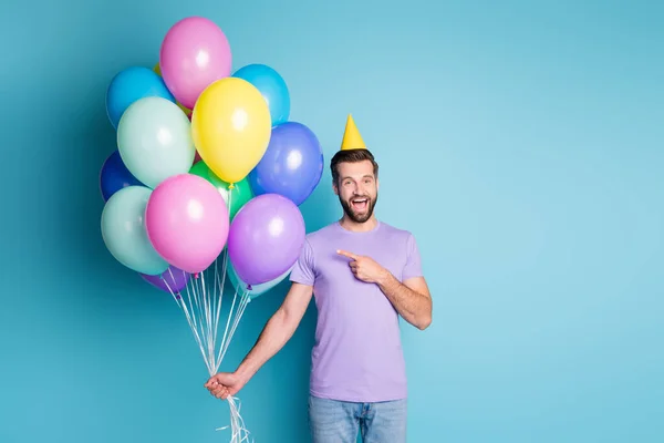 Foto-Porträt von fröhlichen glücklichen Mann zeigt auf Luftballons in festlichen Kegel feiert Geburtstagsparty isoliert auf lebendigen Farbhintergrund — Stockfoto