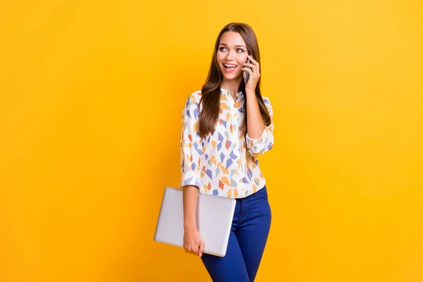 Fénykép portré nő gazdaság laptop az egyik kezében beszél telefonon izolált élénk sárga színű háttér — Stock Fotó