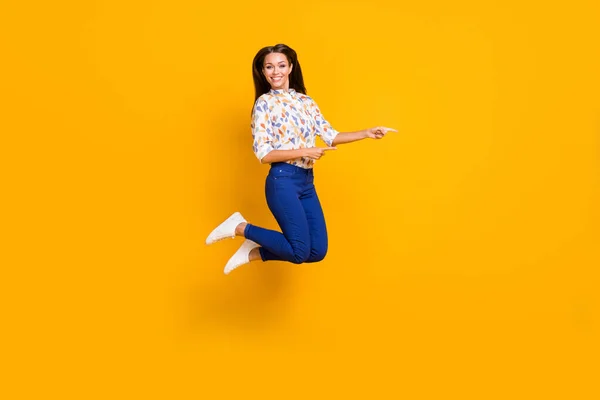 Retrato fotográfico de larga duración de una chica apuntando con dos dedos al espacio en blanco saltando aislada sobre un fondo de color amarillo vivo —  Fotos de Stock