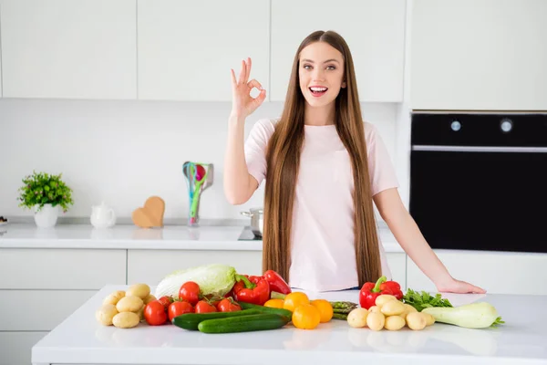 Πορτρέτο της ελκυστική χαρούμενη μακριά μαλλιά κορίτσι μαγείρεμα φρέσκο φυσικό δείπνο δείχνει ok-σημάδι στο σπίτι φως λευκό κουζίνα επίπεδη σπίτι σε εσωτερικούς χώρους — Φωτογραφία Αρχείου