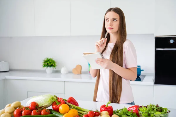 Retrato de mente atraente menina de cabelos compridos escrevendo lista de tarefas cozinhar prato vegan na cozinha casa branca clara dentro de casa — Fotografia de Stock