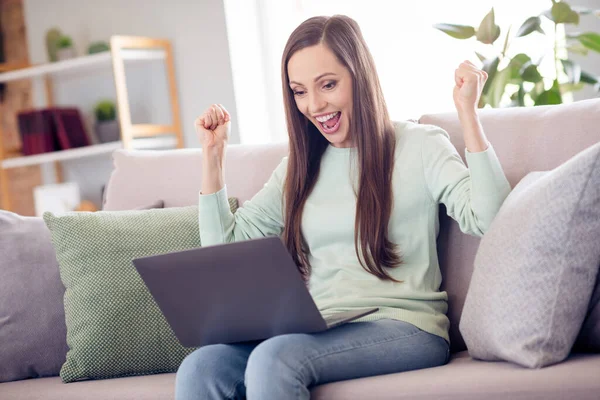 Photo of hooray young brunette lady sit on sofa with laptop wear blue shirt at home alone — Foto Stock