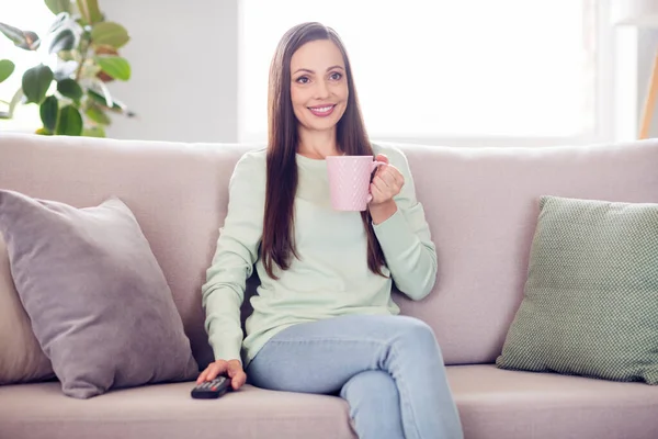 Фото прекрасной брюнетки тысячелетия леди сидеть на диване пить чай смотреть телевизор носить голубую рубашку дома в одиночку — стоковое фото