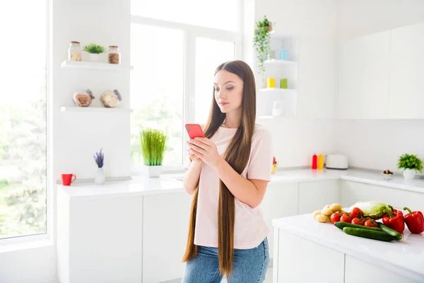 Retrato de chica atractiva enfocada de pelo largo preparando comida doméstica utilizando el dispositivo de búsqueda en el hogar luz blanca cocina interior — Foto de Stock