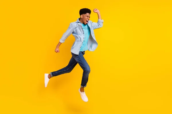 Foto de engraçado apressando cara pele escura vestido camisa jeans correndo rápido saltando alto isolado cor amarela fundo — Fotografia de Stock