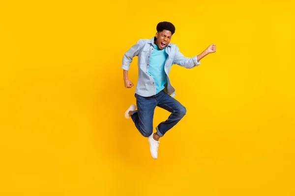 Foto do homem de pele escura animado funky usar camisa jeans saltando alto correndo rápido isolado cor amarela fundo — Fotografia de Stock