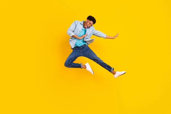 Foto de fresco divertido chico de piel oscura camisa de mezclilla vestida practicando karate saltar alto aislado color amarillo fondo —  Fotos de Stock