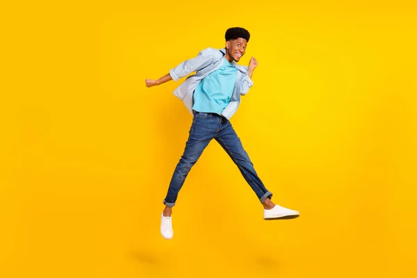 Foto van gelukkige funky donkere huid man dragen jeans shirt springen hoog stijgende vuisten glimlachen geïsoleerde gele kleur achtergrond — Stockfoto