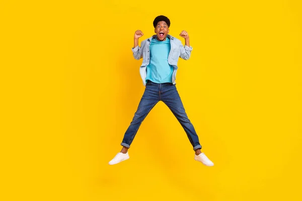 Photo of sweet lucky dark skin man wear jeans shirt jumping high rising fists smiling isolated yellow color background — 图库照片