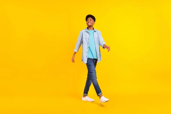 Foto de guapo atractivo chico de piel oscura vestido camisa de mezclilla caminando buscando espacio vacío aislado color amarillo fondo — Foto de Stock