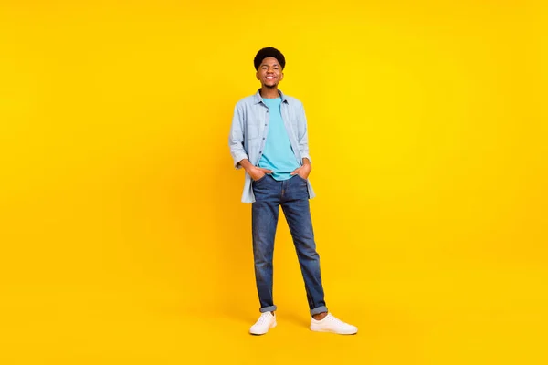 Photo of attractive funny dark skin guy dressed denim shirt walking hands arms pockets smiling isolated yellow color background — Fotografia de Stock