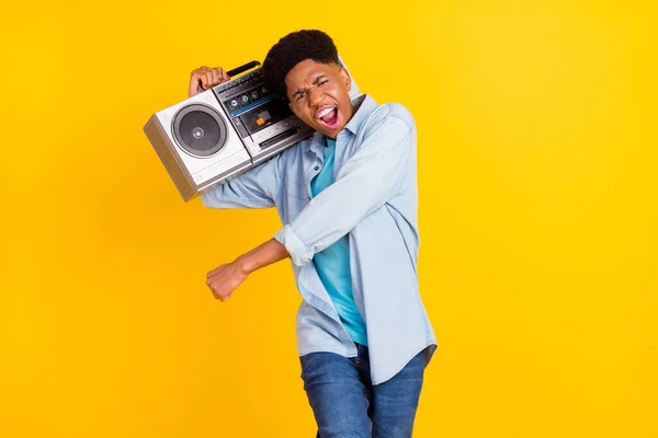 Foto de divertido chico de piel oscura dulce vestido camisa de mezclilla sonriente bailando cantando escuchando boom box aislado color amarillo fondo —  Fotos de Stock