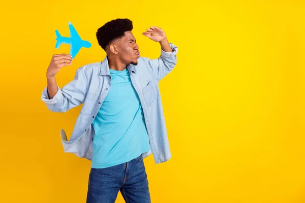 Photo of sweet funny dark skin guy dressed denim shirt holding pane card looking far away empty space isolated yellow color background — Stockfoto