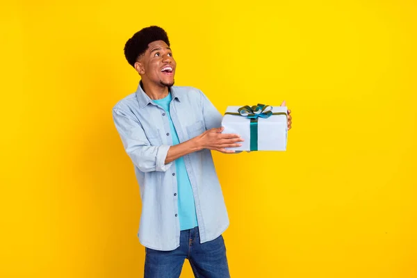 Foto von ziemlich schockiert dunkelhäutige Mann tragen Jeans-Shirt suchen leeren Raum hält Geschenk lächelt isoliert gelbe Farbe Hintergrund — Stockfoto
