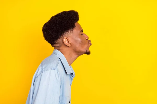 Photo of flirty sweet dark skin guy dressed denim shirt sending kiss empty space isolated yellow color background — стоковое фото