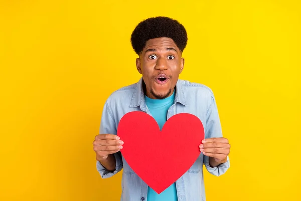 Foto de piel oscura excitada funky hombre usar jeans camisa sosteniendo gran corazón rojo aislado color amarillo fondo —  Fotos de Stock